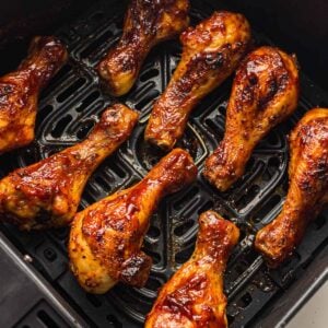 Eight glazed chicken drumsticks are arranged in a single layer inside the basket of an air fryer, cooked to a golden brown.