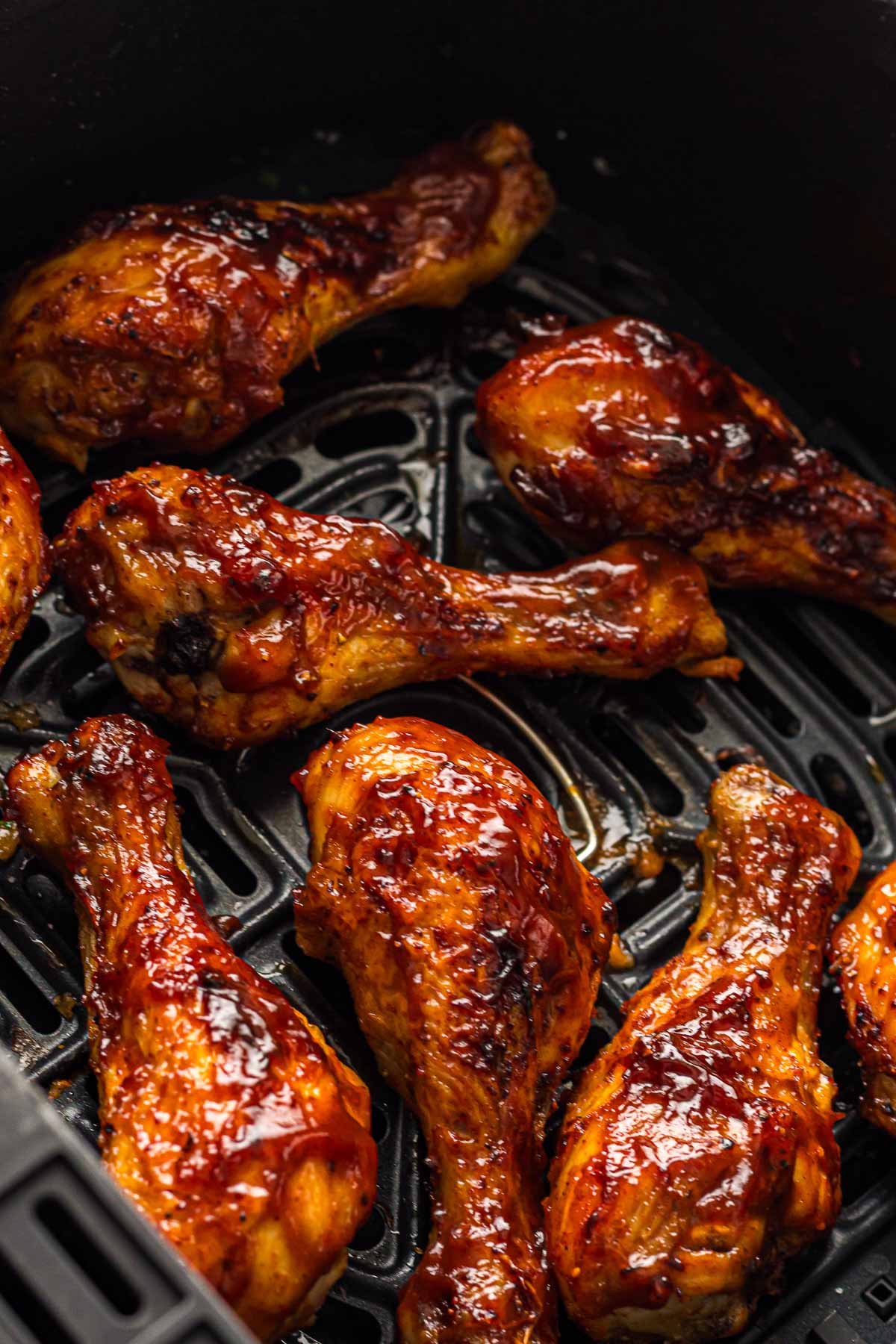 BBQ chicken drumsticks coated in a glossy barbecue sauce are arranged in an air fryer basket.