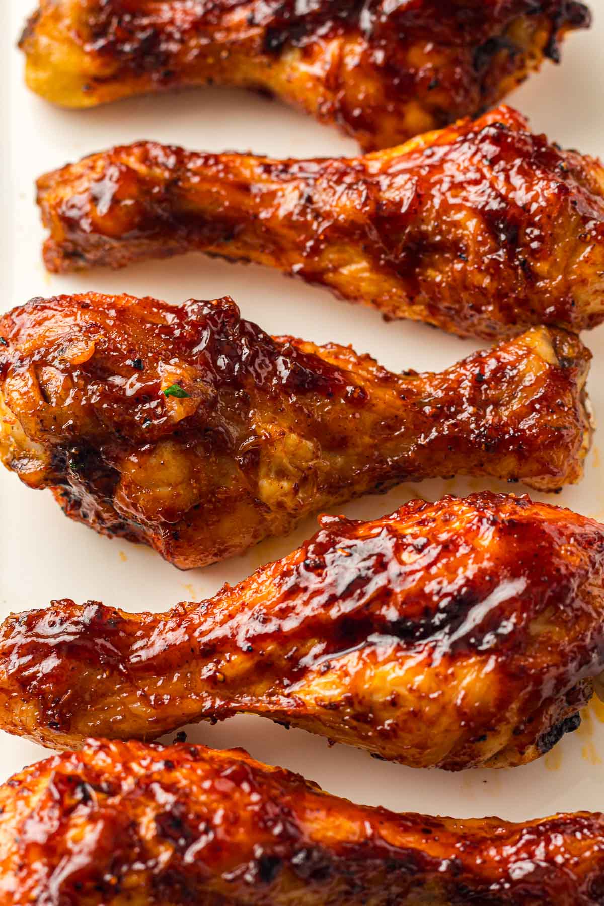 Five Air fried BBQ chicken drumsticks arranged in a row on a white surface.