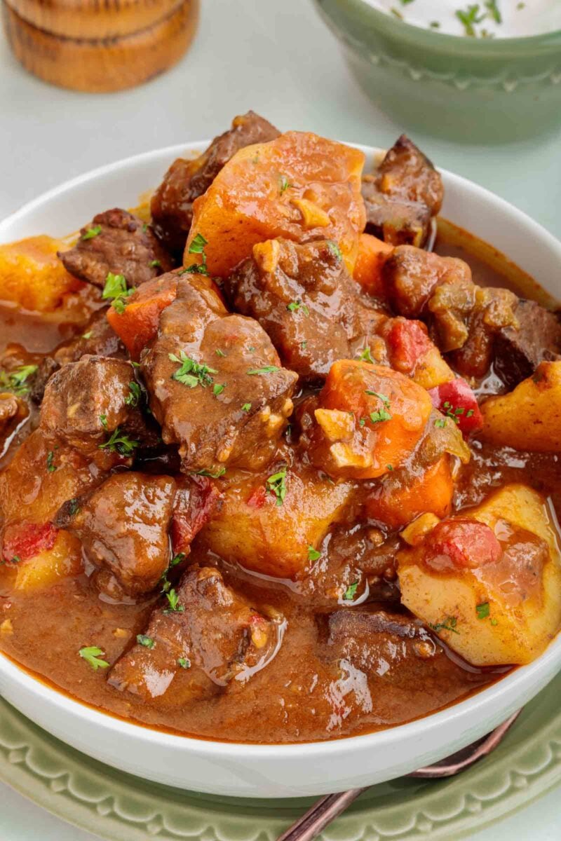 A bowl of beef stew with chunks of beef heart, potatoes, carrots, and a rich brown broth, garnished with chopped parsley.