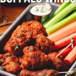A tray of boneless buffalo wings garnished with herbs, served with celery sticks, carrot sticks, and a cup of dipping sauce.