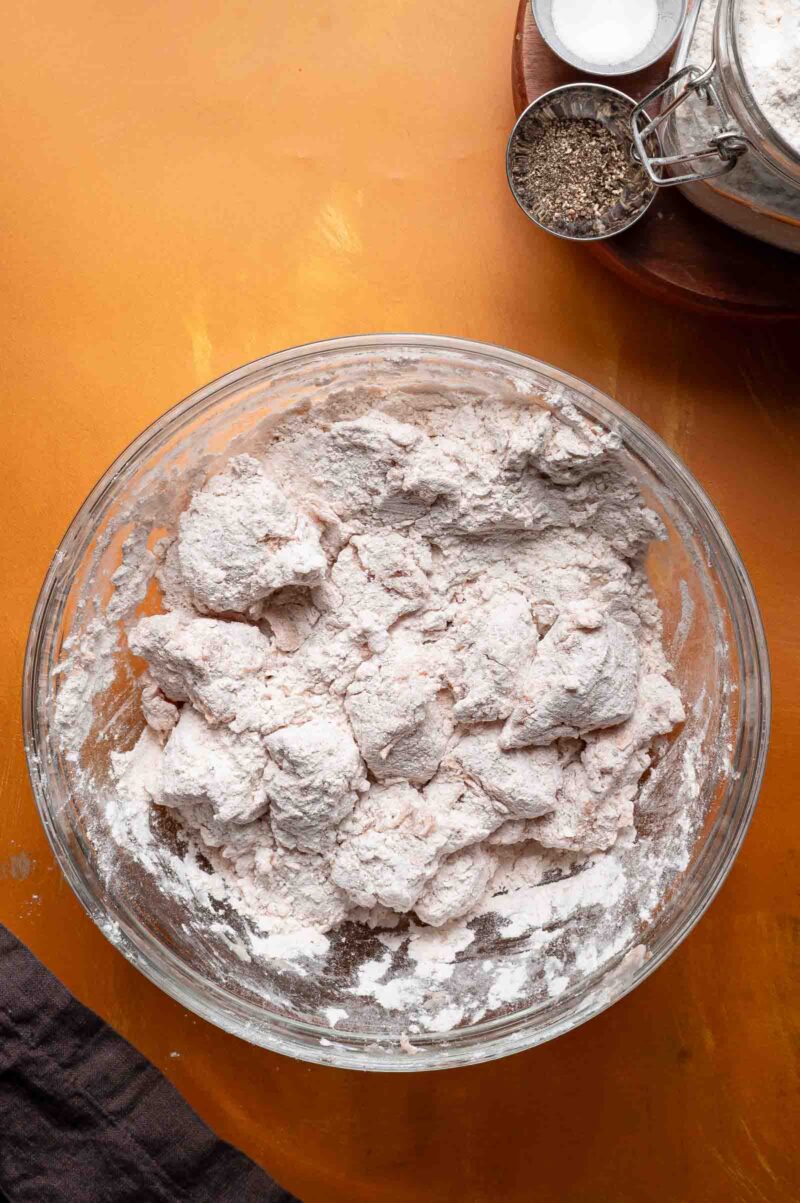 A bowl of flour coated chicken pieces on a table.
