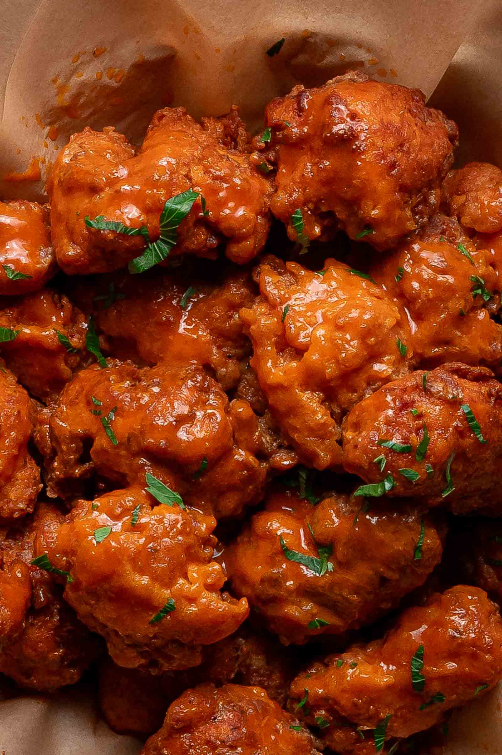 A close-up of saucy buffalo chicken wings garnished with chopped parsley on parchment paper.