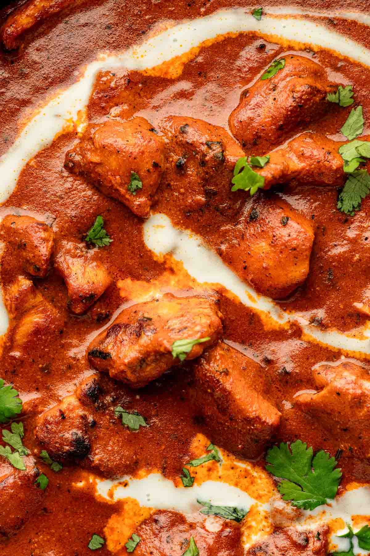 Close-up of butter chicken in a creamy tomato sauce, garnished with fresh cilantro and a swirl of cream.