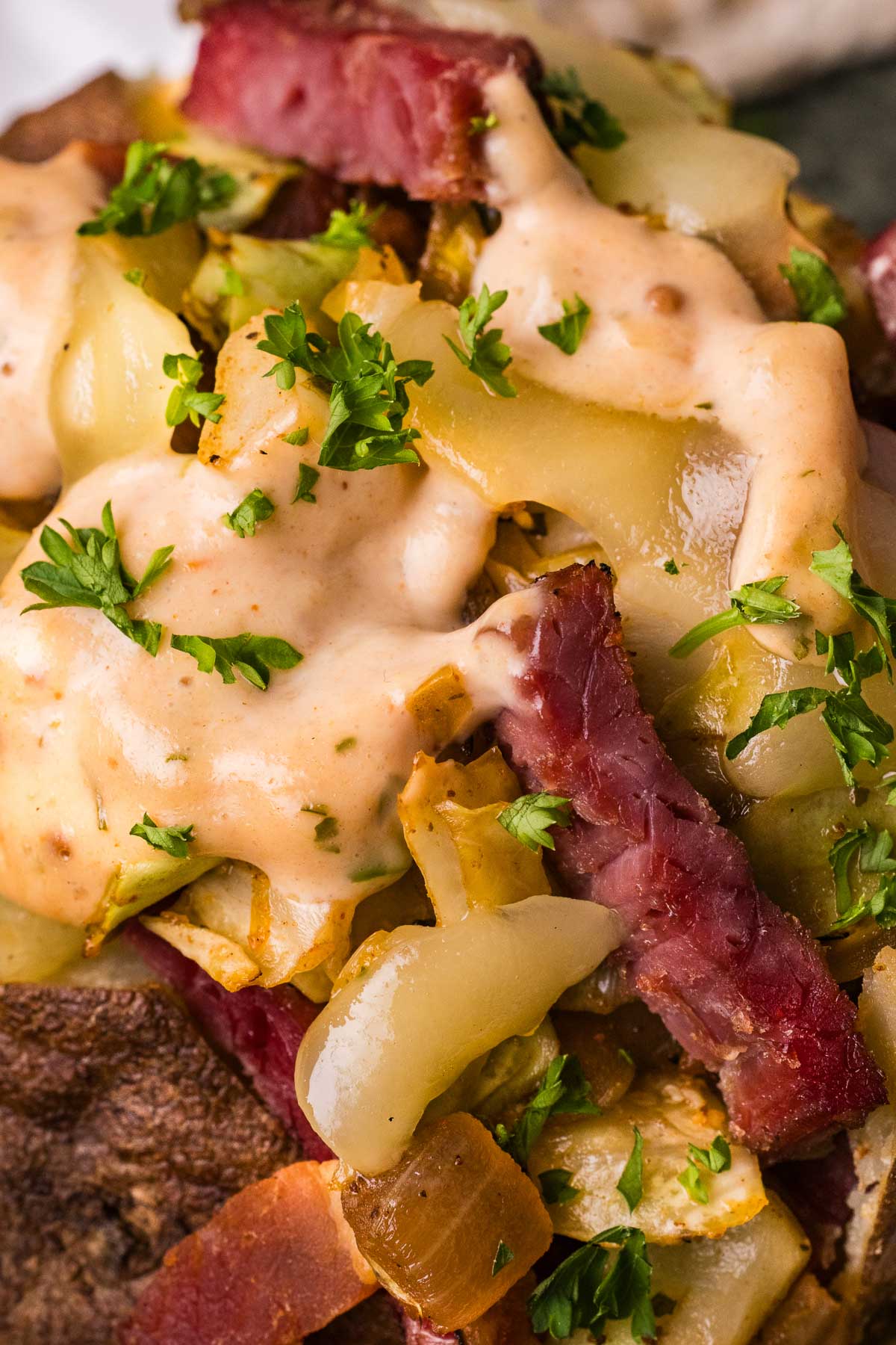 Close-up of a smoked stuffed baked potato with sliced corned beef, sautéed cabbage, reuben dressing, and chopped parsley on top.