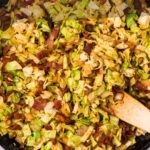 A skillet filled with fried cabbage and bacon pieces being stirred with a wooden spatula. Text overlay reads, "How to make fried cabbage with bacon.