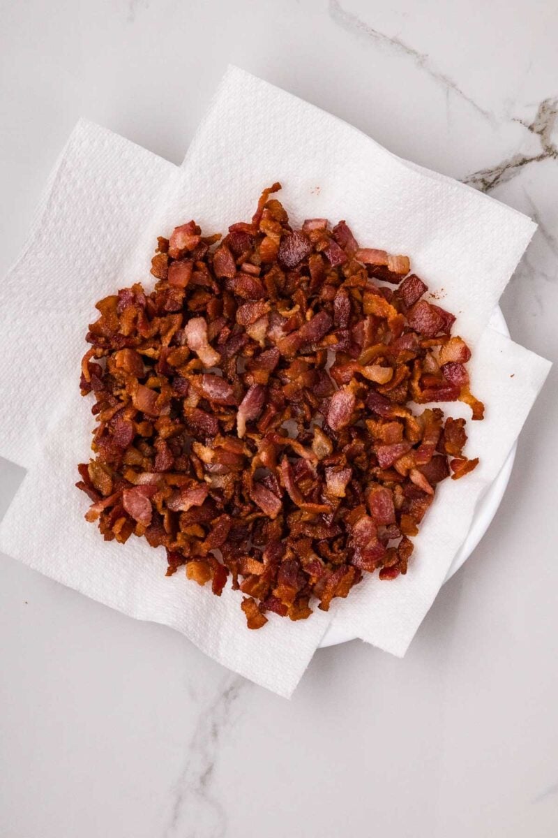 Chopped cooked bacon pieces on paper towels atop a white plate on a marble surface.