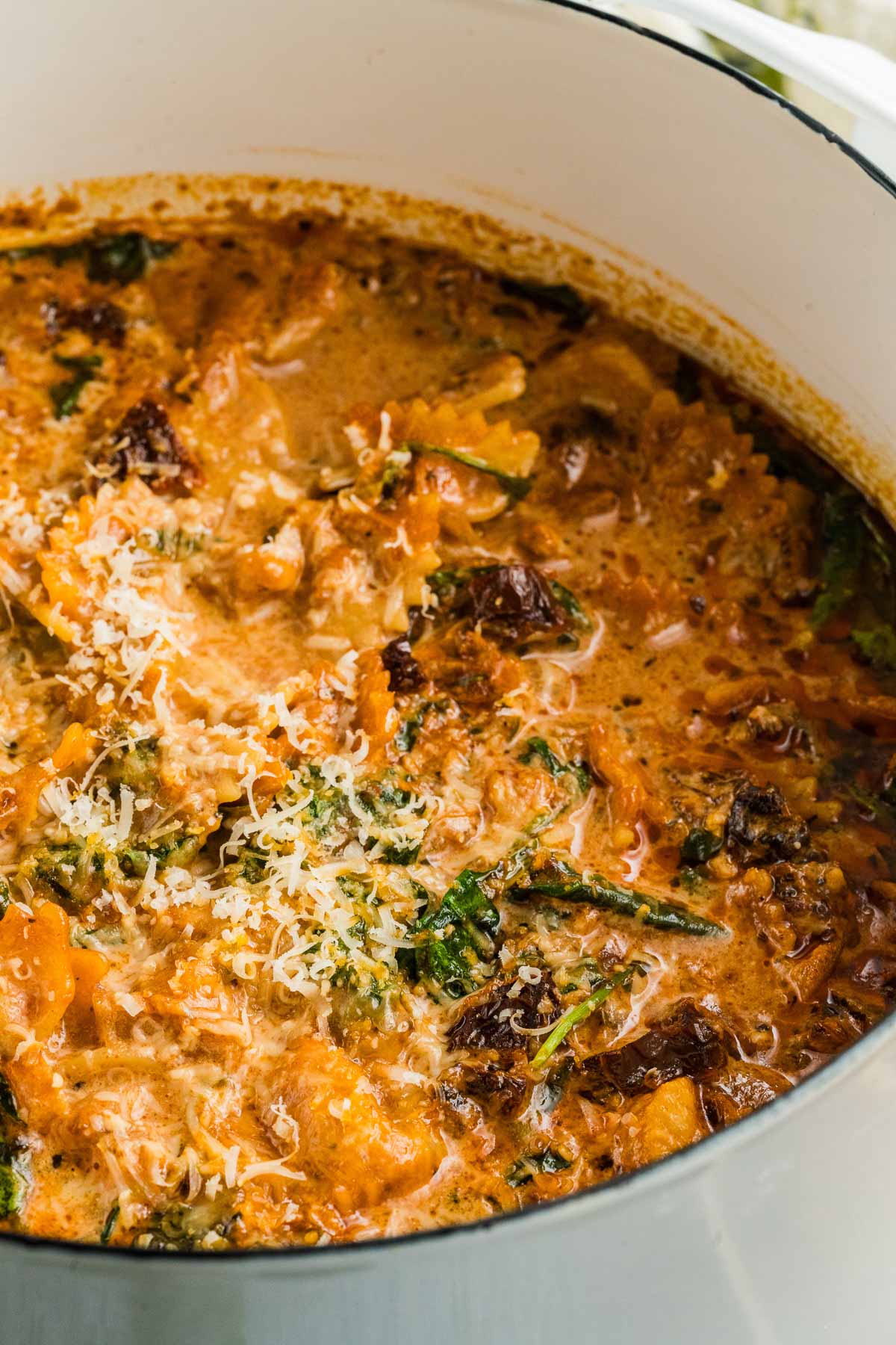 A close-up of a creamy marry me chicken soup with visible spinach, shredded chicken, sun-dried tomatoes, and grated cheese in a white pot.
