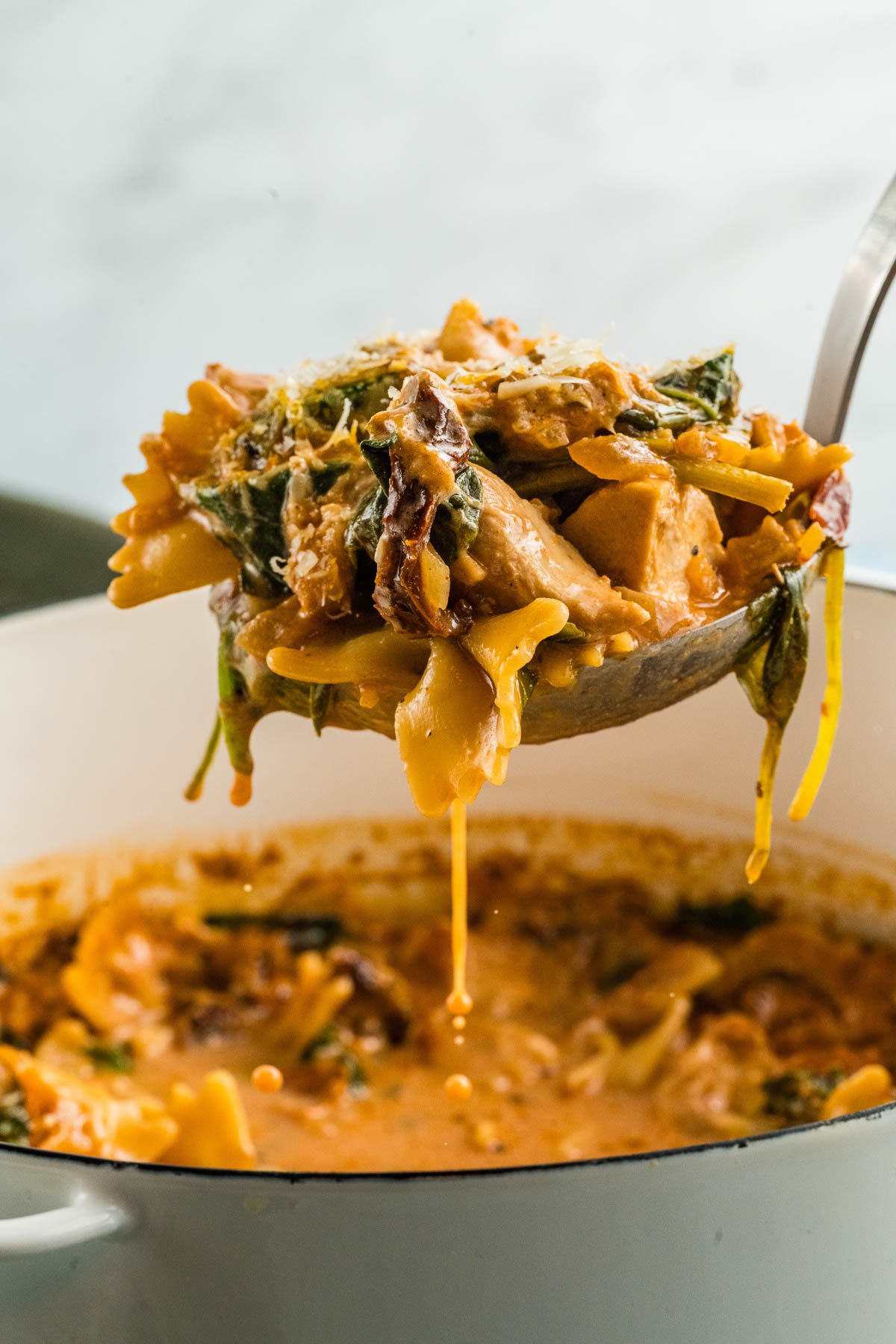 A ladle lifts creamy marry me chicken soup with spinach, chicken, and sauce from a dutch oven.