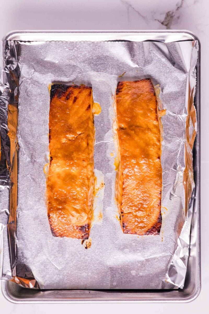 Two fillets of cooked salmon with a golden miso glaze on a foil-lined baking sheet.