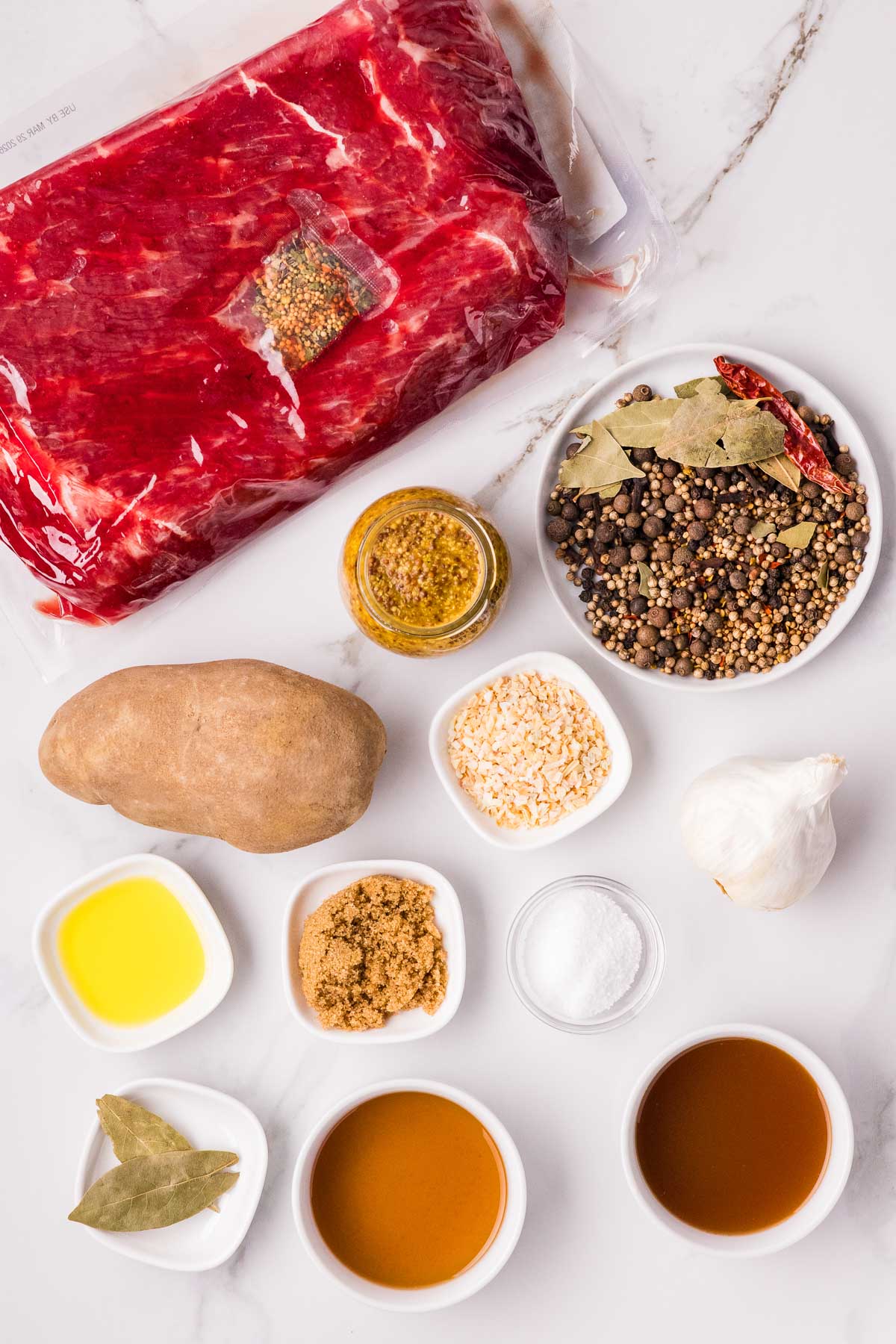 Raw corned beef in packaging, spices, a potato, garlic, mustard, oil, brown sugar, salt, and liquids arranged on a white marble surface.