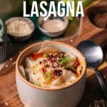 A bowl of viral dumpling lasagna topped with chili oil and green onions, placed on a wooden board with dumpling wrappers and utensils nearby.