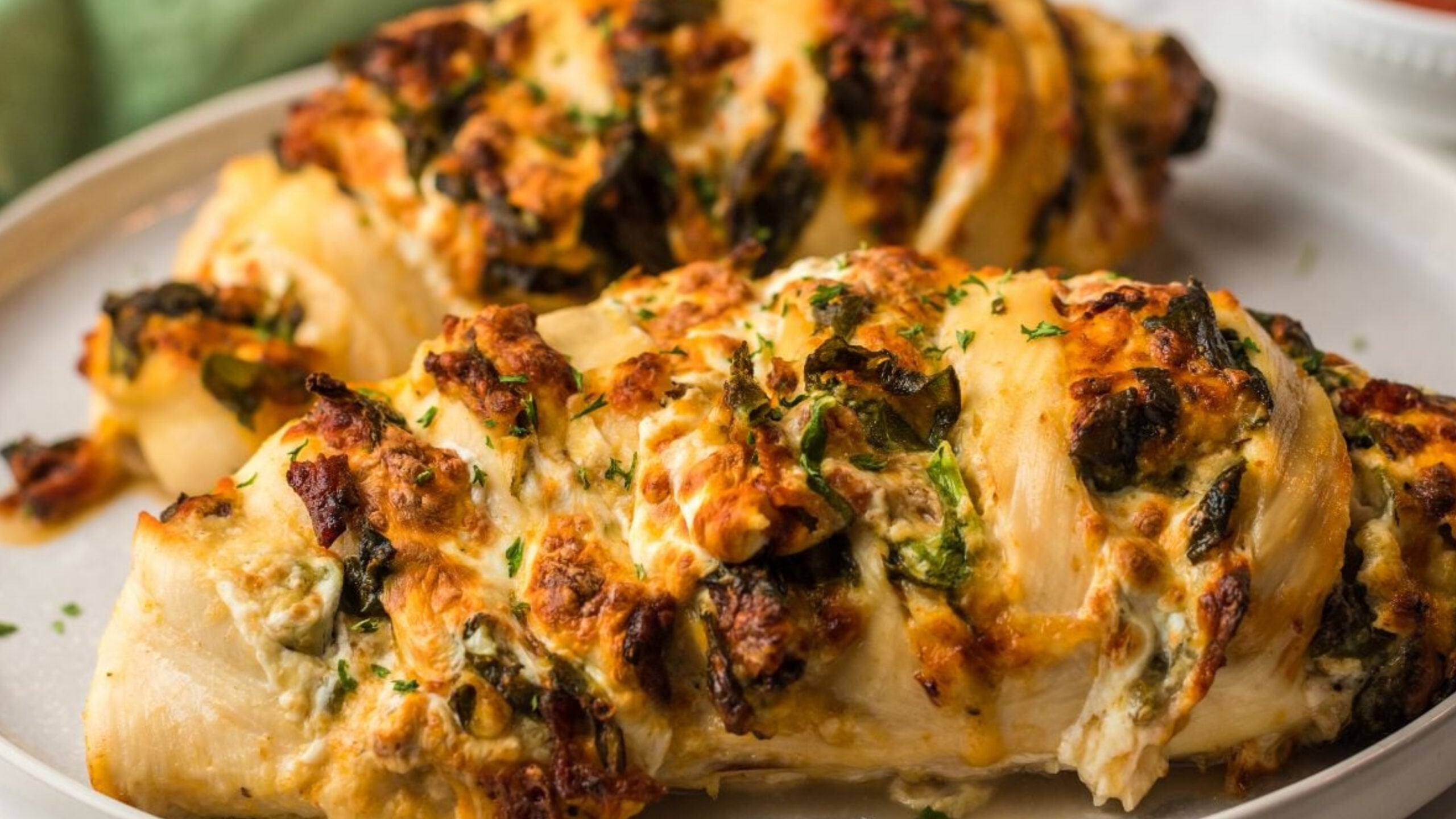 Large stuffed pasta shells filled with greens and cheese, topped with melted browned cheese and chopped herbs on a plate.