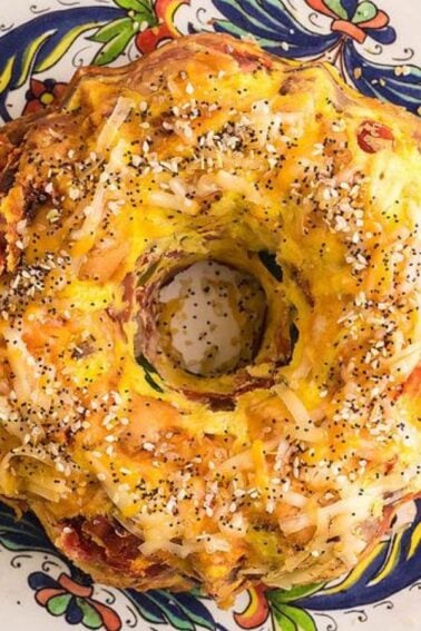 A savory bundt cake topped with shredded cheese and seeds sits on a decorative plate with spinach leaves arranged underneath.