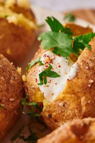 Baked potatoes topped with sour cream, chopped parsley, and sprinkled spices are arranged on a plate.