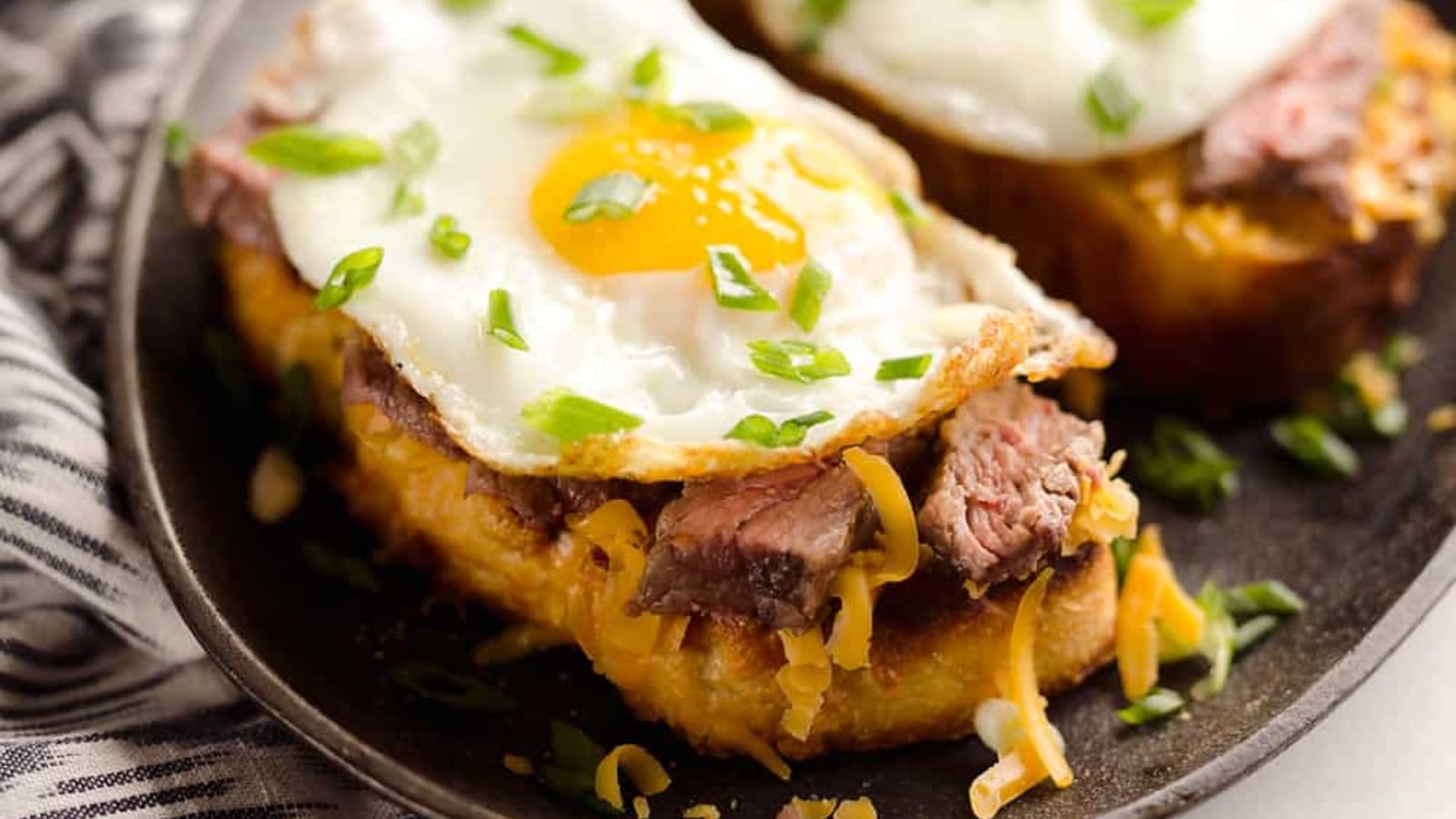 Steak and cheddar breakfast toasts with melted cheese over sliced steak on toasted bread.