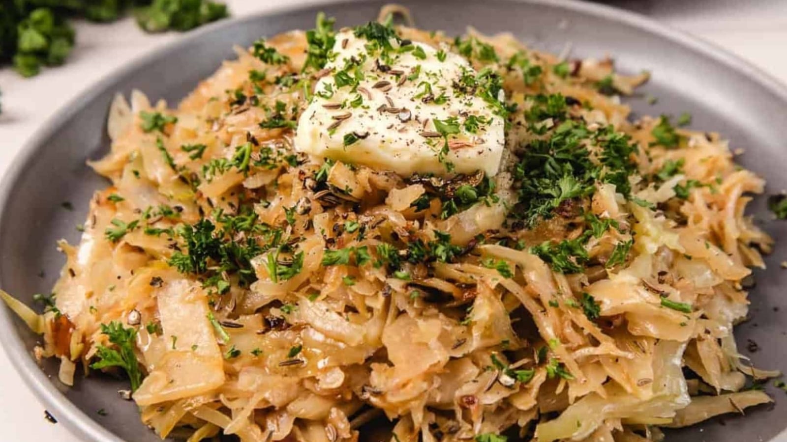 Shredded sautéed cabbage with herbs and a pat of butter on top, served on a gray plate.