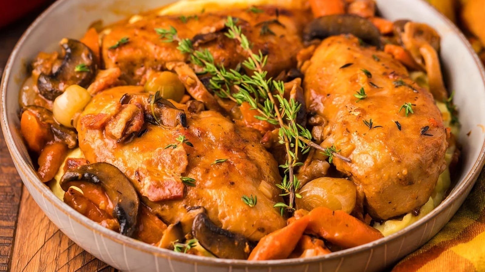 A dish of cooked chicken breasts with mushrooms, carrots, onions, and herbs in a brown sauce, served in a shallow bowl.