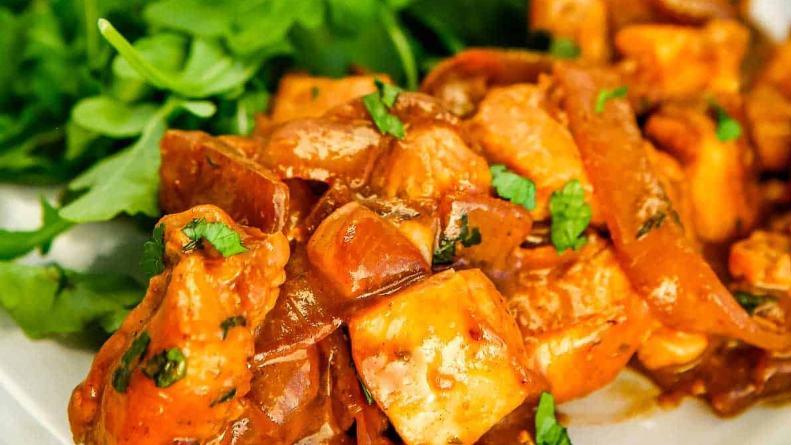 Close-up of paneer tikka masala garnished with chopped cilantro, served with a side of fresh green salad leaves.