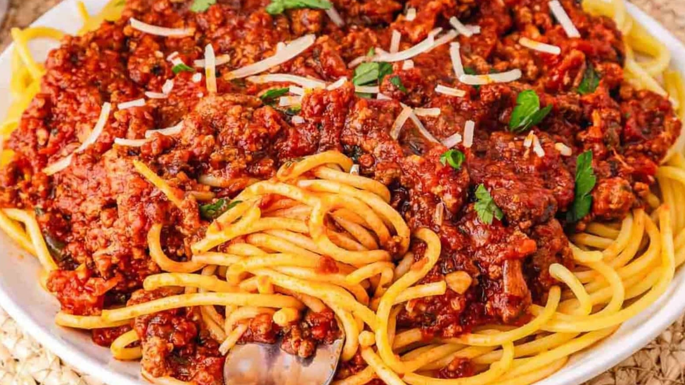 A plate of spaghetti topped with chunky meat sauce and garnished with grated cheese and parsley.