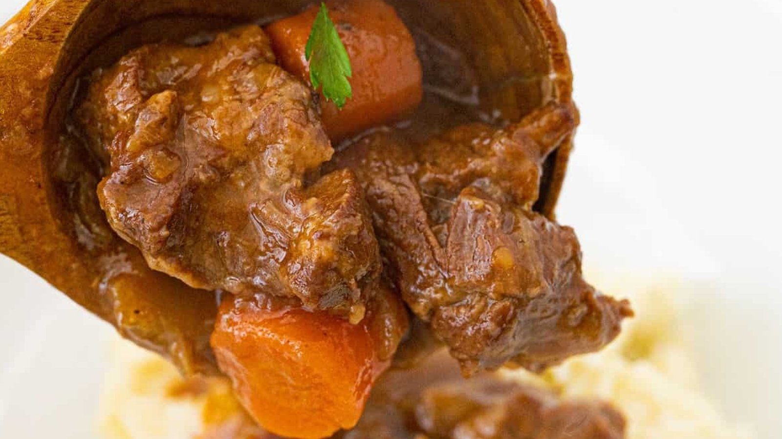 A close-up of beef stew with chunks of beef and carrots in brown gravy, being served over mashed potatoes.