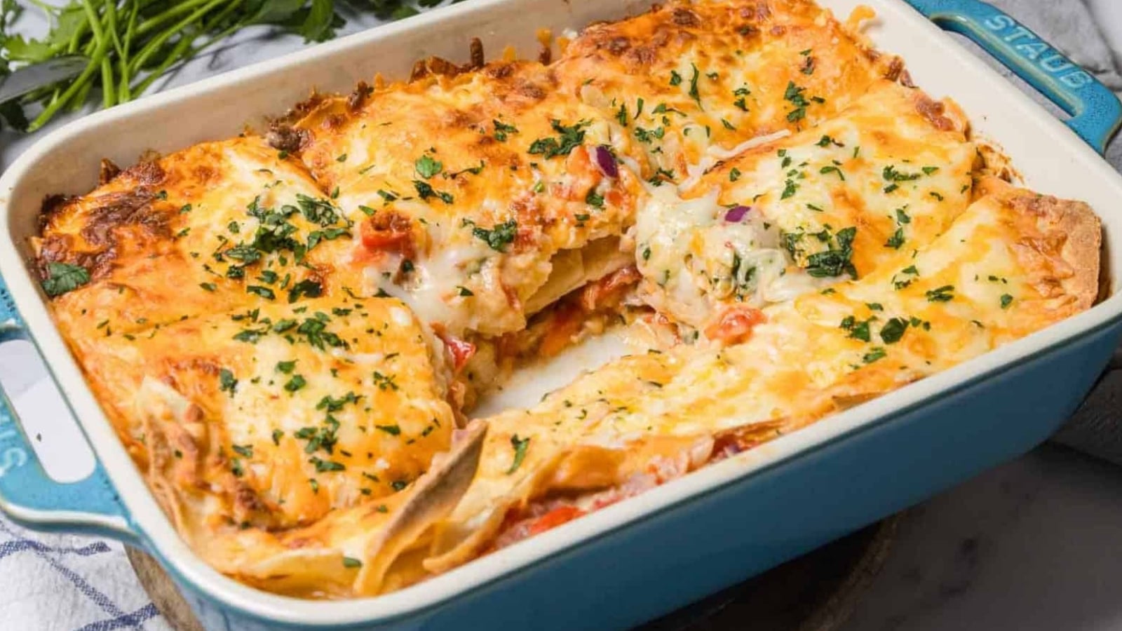 A cheesy baked lasagna in a blue dish, with a square piece removed and herbs sprinkled on top.