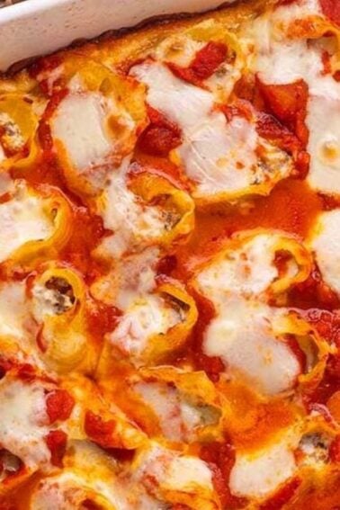 A baked dish of stuffed pasta shells topped with tomato sauce and melted cheese in a white rectangular baking pan.