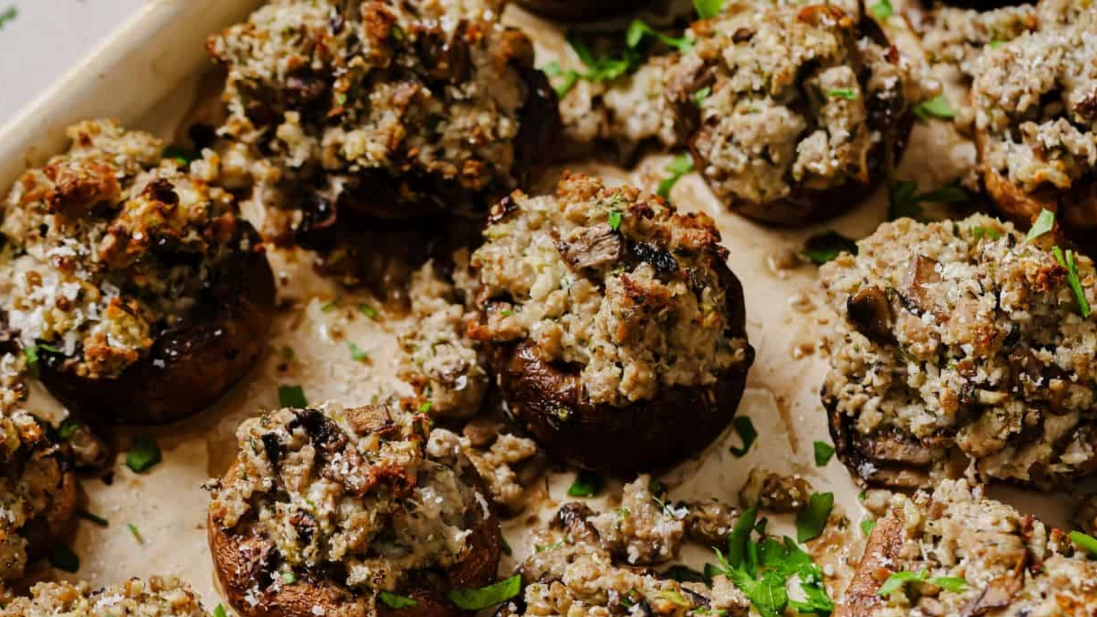 A baking tray filled with stuffed mushrooms topped with a breadcrumb and herb mixture, garnished with chopped parsley.