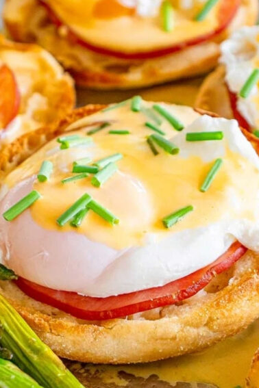English muffins topped with ham, poached eggs, hollandaise sauce, and chopped chives, served with a side of asparagus spears.