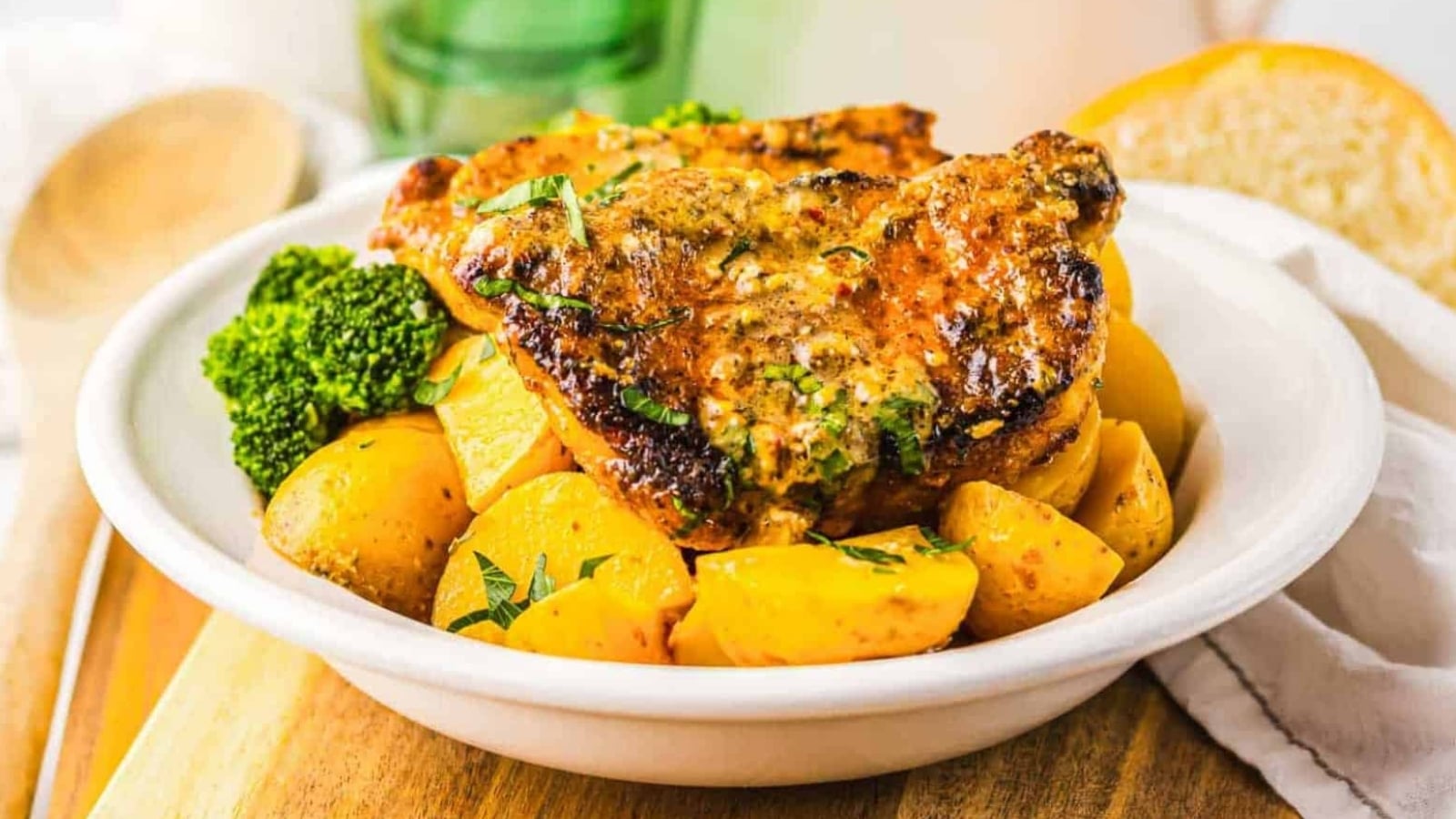 Grilled pork chops with roasted potatoes and broccoli served in a white bowl on a wooden surface.