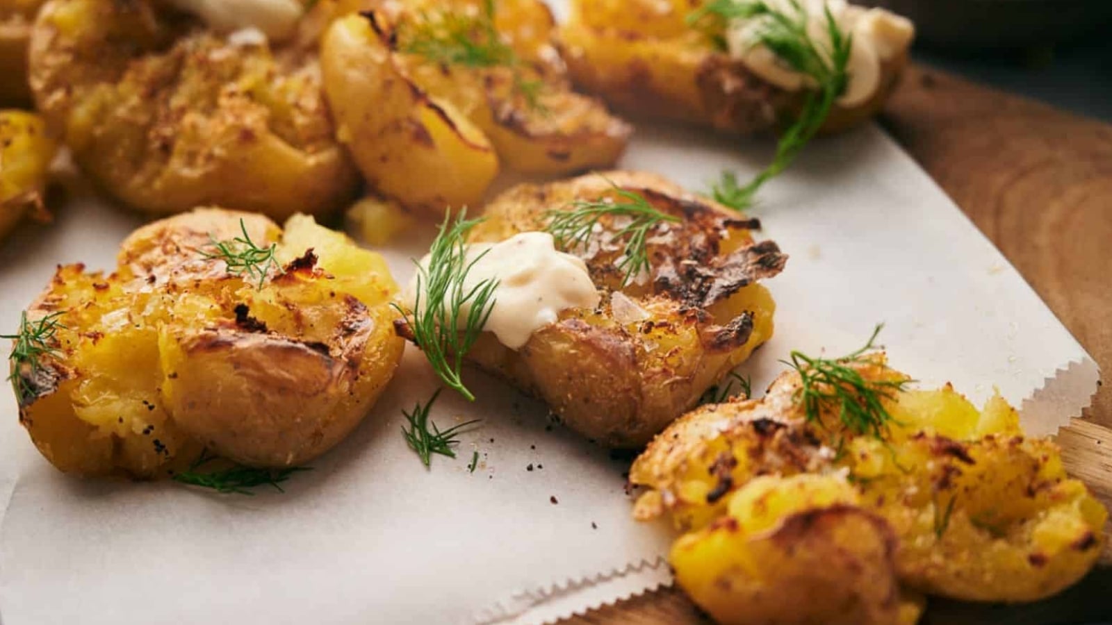 Smashed potatoes on parchment paper, with dollops of sauce and sprigs of dill.