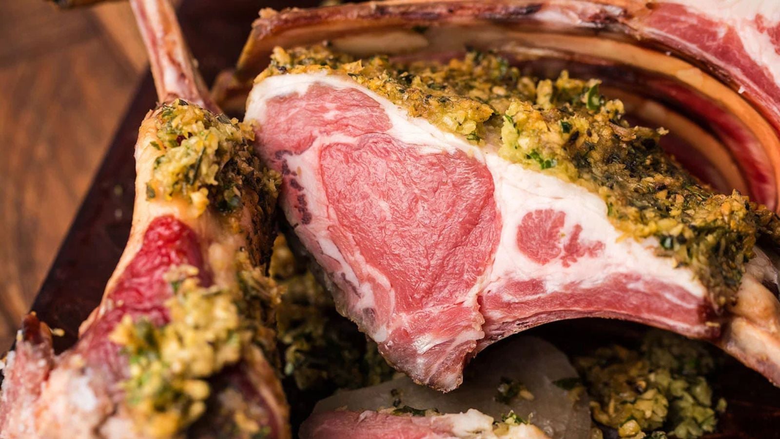 Close-up of a rack of lamb, sliced to show the pink meat inside, coated with a green herb and breadcrumb crust.