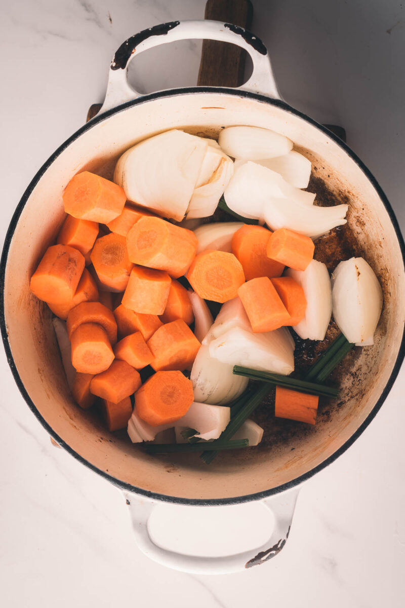 A white pot containing chopped carrots, onions, and celery on a white surface.