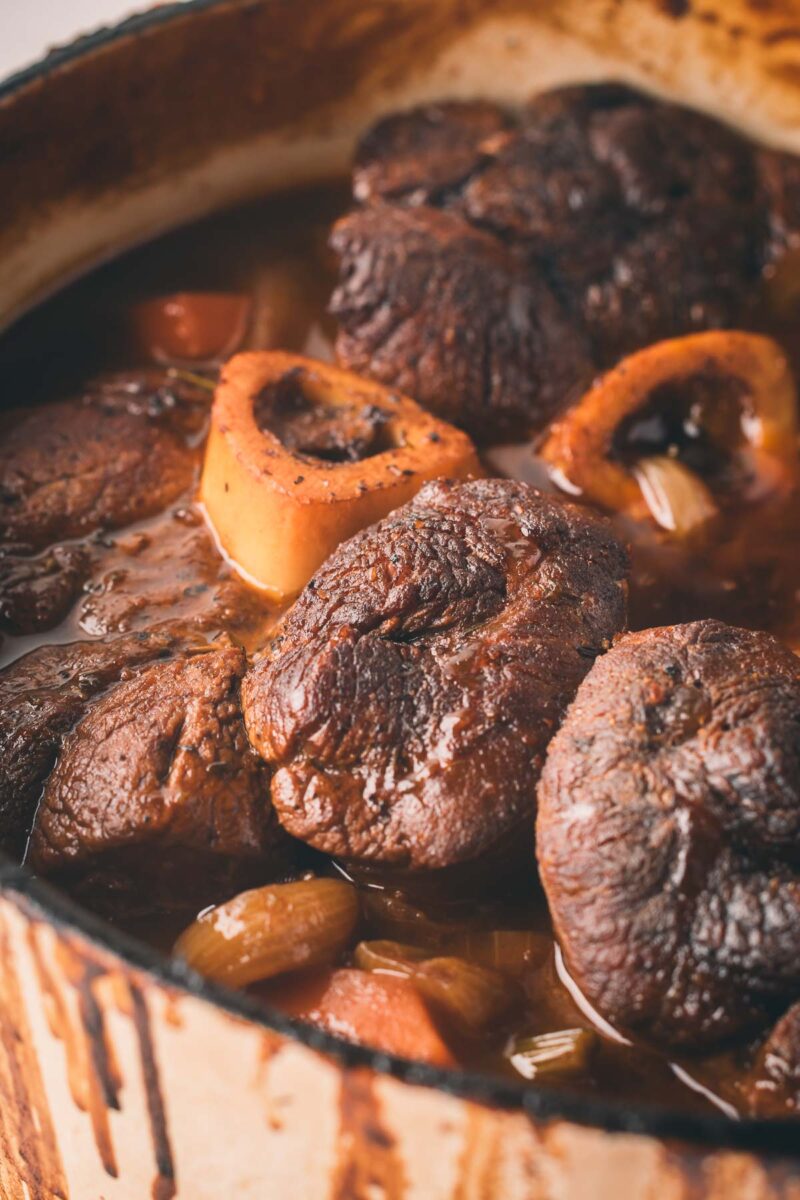 A close-up of braised beef shanks simmering in broth with vegetables in a large pot.