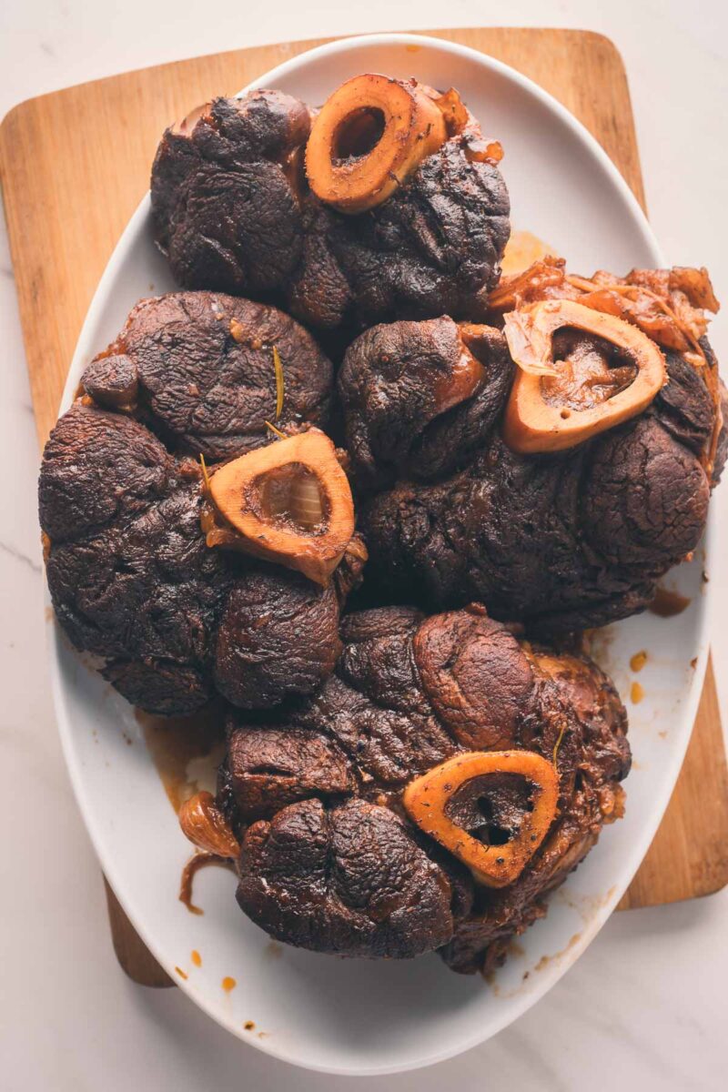 A white oval plate with several pieces of braised beef shank and exposed marrow bones, placed on a wooden cutting board.