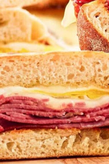 Close-up of sliced sandwiches with layers of corned beef and melted cheese between crusty bread.