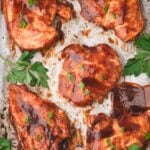 Five pieces of baked BBQ chicken garnished with parsley are arranged on a baking sheet, with a text overlay about making baked BBQ chicken and a website link at the bottom.
