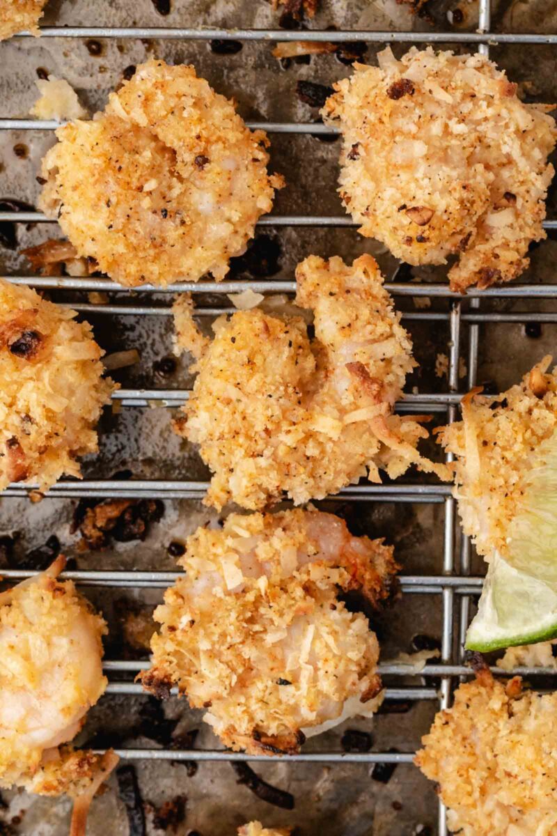 Breaded coconut shrimp on a metal wire rack, with a slice of lime visible in the corner.