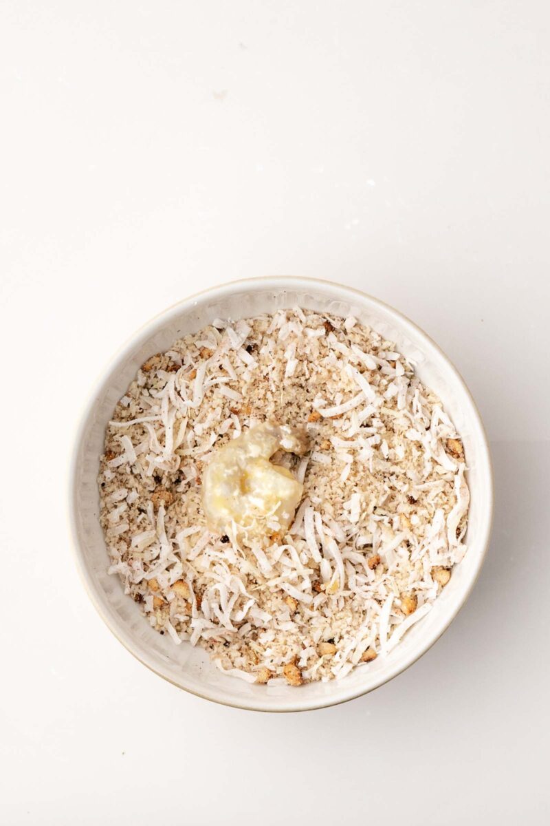 A shrimp being coated in a mixture of coconut, macadamia nuts and breadcrumbs.