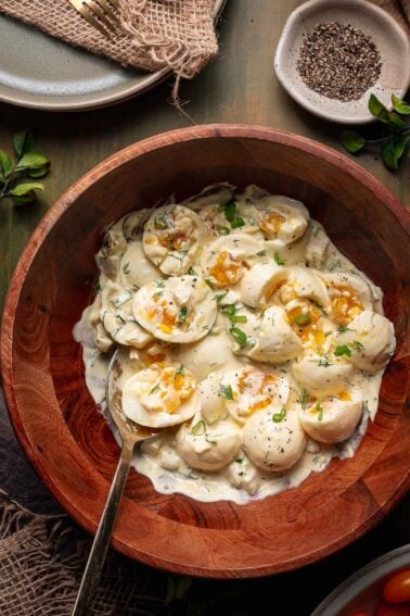 Creamy dilly broken egg salad garnished with chopped green onions and black pepper, served in a wooden bowl with a spoon.