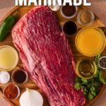 Raw flank steak on a wooden board surrounded by marinade ingredients, including spices, lime, onion, cilantro, and liquids. Text reads, “How to make carne asada marinade.”.