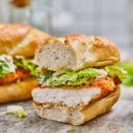 A crispy caesar chicken sandwich with lettuce and sauce, cut in half and displayed on a stone surface with a blurred background.