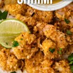 Plate of crispy coconut shrimp garnished with lime slices and cilantro, served with dipping sauce; text overlay reads โHow to Make Coconut Shrimp.โ.