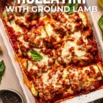 A baked dish of eggplant rollatini with ground lamb, topped with melted cheese and tomato sauce, is shown in a rectangular white baking dish on a table.