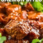 Close-up of glazed salmon bites with honey being drizzled on top, garnished with fresh herbs. Text overlay reads "How to Make Hot Honey Salmon Bites.