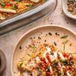 A serving of salmon sushi bake on a plate topped with sauces and herbs, with a baking dish and seasoning bowl nearby. Text reads, "How to make salmon sushi bake.