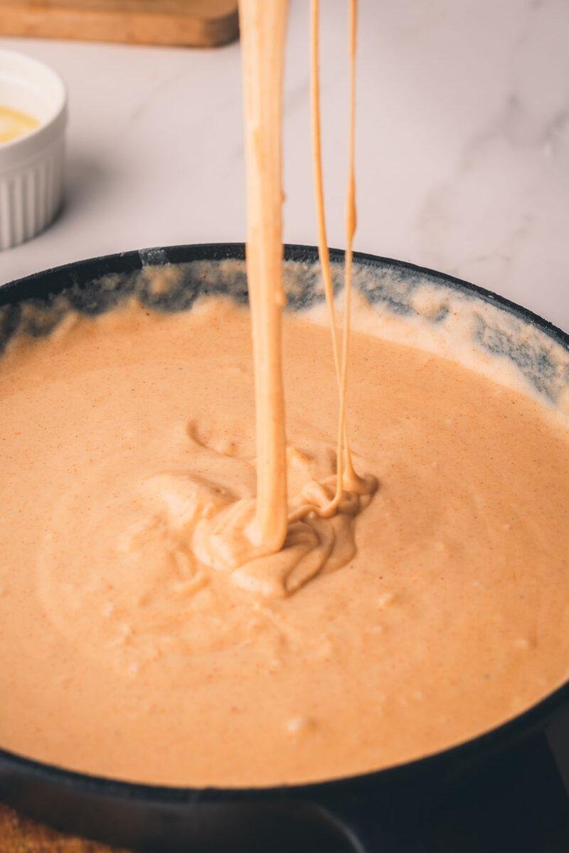 Thick, creamy cheese sauce in a skillet with melted cheese being stretched upward from the center.