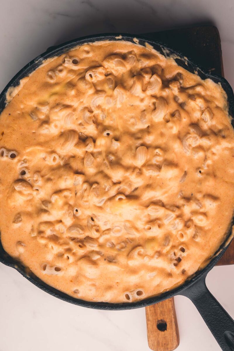 A cast iron skillet filled with creamy macaroni and cheese, resting on a wooden board.