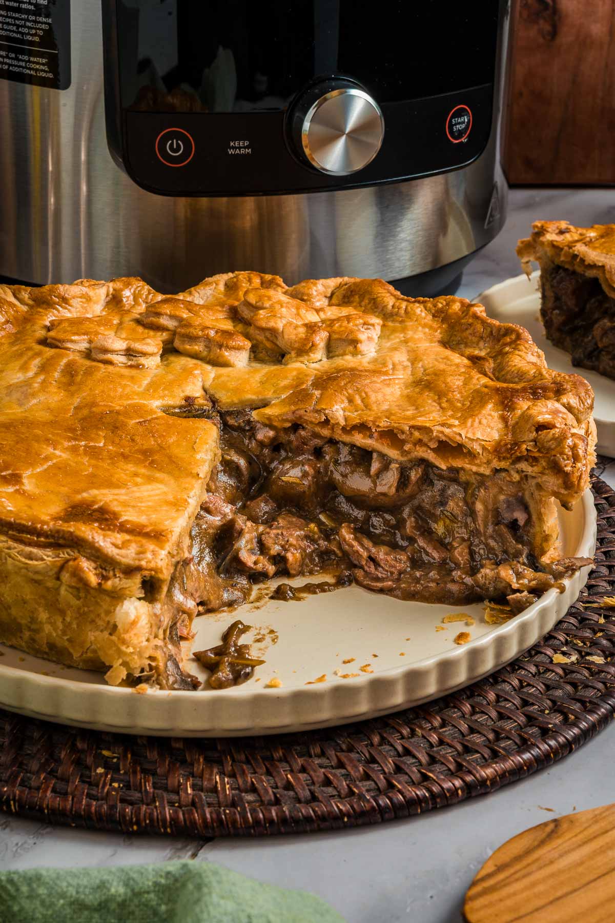 A sliced steak and kidney pie with a golden-brown crust sits on a ceramic plate in front of a kitchen appliance.