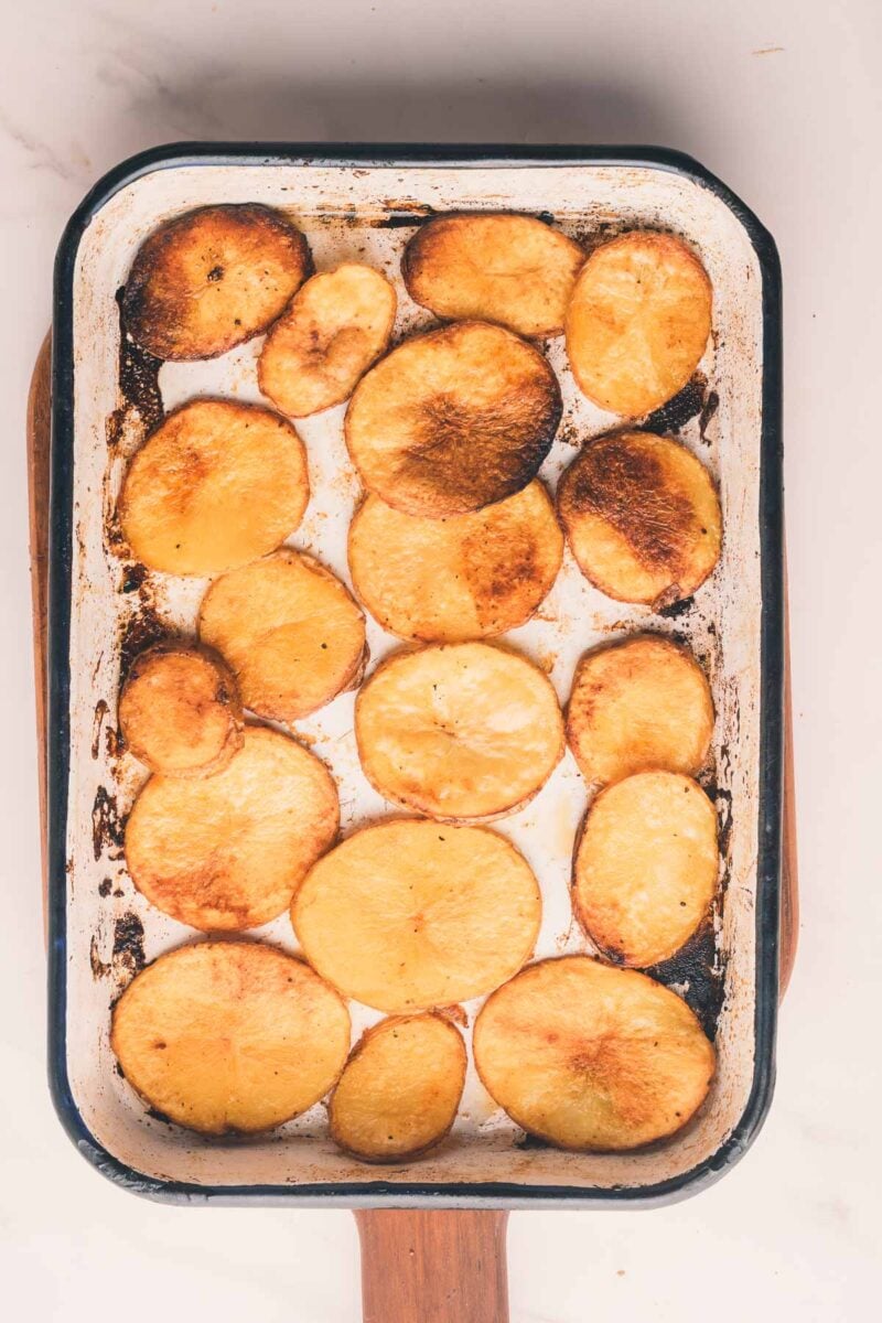 Sliced roasted potatoes arranged in a single layer on a rectangular baking tray with browned edges.